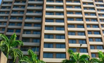 a tall , beige - colored building with many windows and palm trees in front of it , set against a clear blue sky at JW Marriott Hotel Caracas