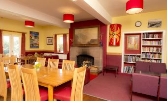a dining room with a wooden table and chairs , a fireplace , and red curtains on the windows at YHA Eskdale