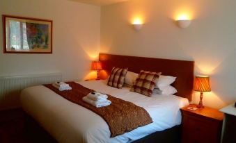 a large bed with a red headboard and white linens is in a room with two lamps on either side at The Fox & Hounds