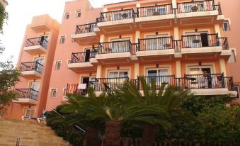 a three - story building with orange and pink exterior , balconies , and palm trees , under a clear blue sky at THB Felip - Adults Only