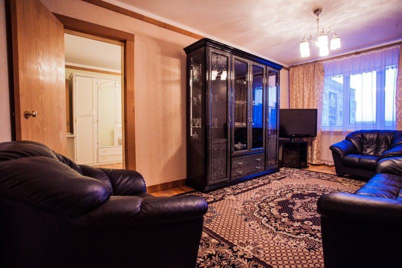 a living room with a black leather couch , wooden entertainment center , and a patterned rug at Norilsk