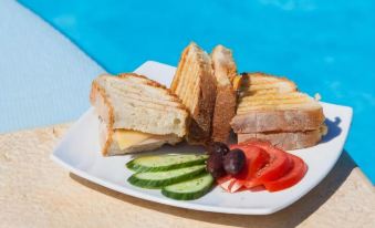 a white plate with a variety of sandwiches , including cucumbers and tomatoes , placed on a dining table near a swimming pool at Amorgion Hotel
