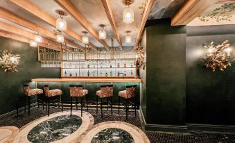 a modern bar with green walls , wooden beams , and marble floors , featuring several stools and a central bar at The Cellars-Hohenort