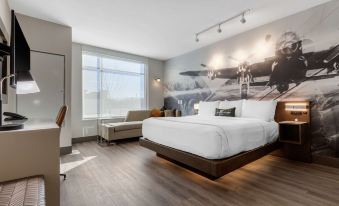 a large bed with white linens is in a room with a wooden floor and a mural on the wall at Cambria Hotel - Arundel Mills BWI Airport