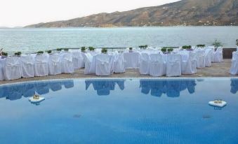 a large outdoor pool surrounded by tables and chairs , with a view of the ocean in the background at Golden View