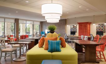 a modern hotel lobby with a yellow couch , blue chairs , and pendant lights hanging from the ceiling at Home2 Suites by Hilton Joliet/Plainfield