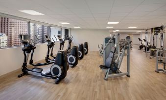 a gym with various exercise equipment , including treadmills and stationary bikes , in a spacious room with large windows at Sheraton Philadelphia Downtown