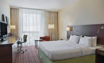 a large bed with white linens is in a room with a striped carpet and a window at Courtyard Basel