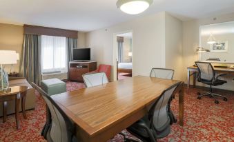 a large wooden dining table surrounded by chairs in a hotel room , with a television and couch visible in the background at Hilton Garden Inn Nanuet