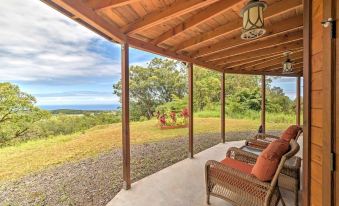 a wooden patio with a view of the ocean , featuring two wicker chairs and a dining table at Hawaiian Hideaway at Akaka Falls