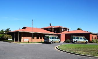 two buses are parked in front of a brick building with a red roof , under a clear blue sky at Peppermill Inn Motel