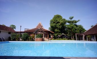 a large swimming pool with a house in the background and trees surrounding it at Griya Gendhis Saraswati