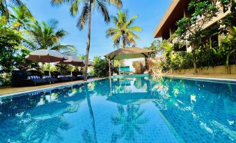 a large outdoor swimming pool surrounded by palm trees , with lounge chairs and umbrellas placed around the pool area at Riva Beach Resort