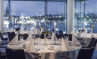 a well - lit dining room with a table set for a formal event , surrounded by large windows offering a view of the city at Radisson Blu Waterfront Hotel, Stockholm