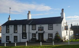a white and black building with a red roof , situated in a grassy area near a tree at The Shepherds Inn