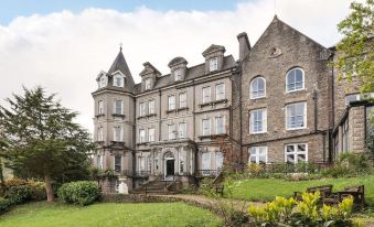 a large , gray stone mansion with multiple windows and balconies , surrounded by lush green grass and trees at The Valley of Rocks Hotel