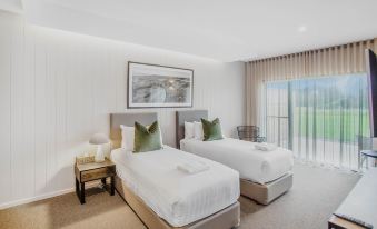a modern bedroom with two beds , a window , and a painting on the wall , all decorated in white and beige colors at 13th Beach Golf Lodges