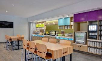 a modern cafeteria with wooden tables and chairs , a counter , and a tv in the background at Home2 Suites by Hilton Fort Mill