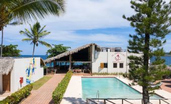 a resort with a pool surrounded by palm trees , and a building with a thatched roof at Hotel Bocaino