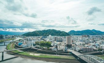 a cityscape with a large body of water in the foreground , surrounded by buildings and mountains at Numazu River Side Hotel