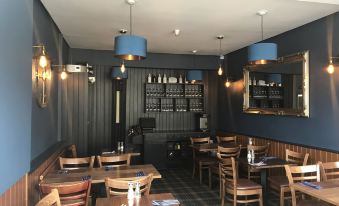 a modern restaurant interior with wooden tables , blue pendant lights , and wine storage racks behind the dining tables at Aberdour Hotel, Stables Rooms & Beer Garden