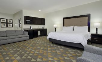 a modern hotel room with a large bed , couch , and kitchen area , all decorated in neutral colors at Holiday Inn Hammond
