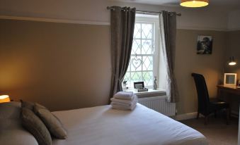 a neatly made bed with white linens and a window view of a radiator , next to a chair and a lamp at The Punchbowl Hotel