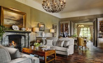 a spacious living room with a large couch , a dining table , and a fireplace , decorated with pictures on the walls at Ballynahinch Castle Hotel