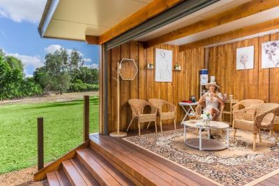 a woman sitting in a chair on a deck with a view of the grass and trees at The Swan Valley Retreat