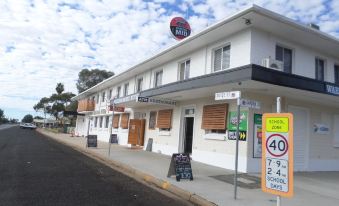 a large building with a red sign on top , located on a street corner in a small town at Warrego Hotel Motel Cunnamulla