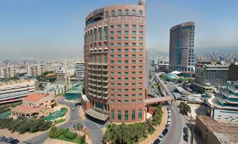 a tall , modern building with a red brick exterior and green windows is surrounded by other buildings and roads in a city at Hilton Beirut Metropolitan Palace