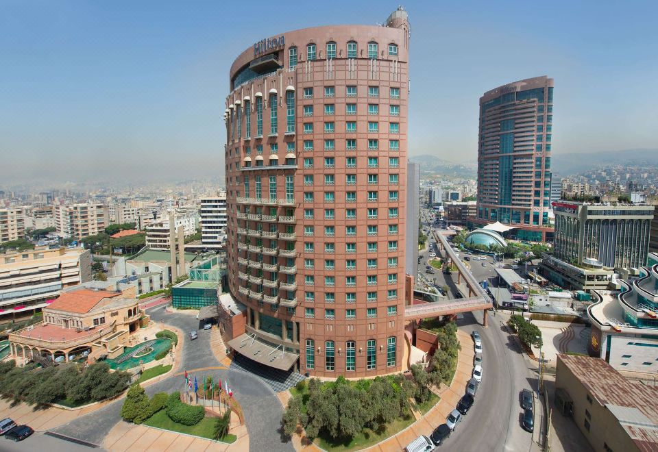 a tall , modern building with a red brick exterior and green windows is surrounded by other buildings and roads in a city at Hilton Beirut Metropolitan Palace