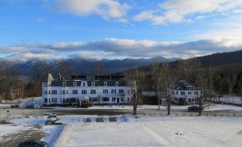 a large white building surrounded by snow - covered trees and mountains , creating a serene winter landscape at Sunset Hill House