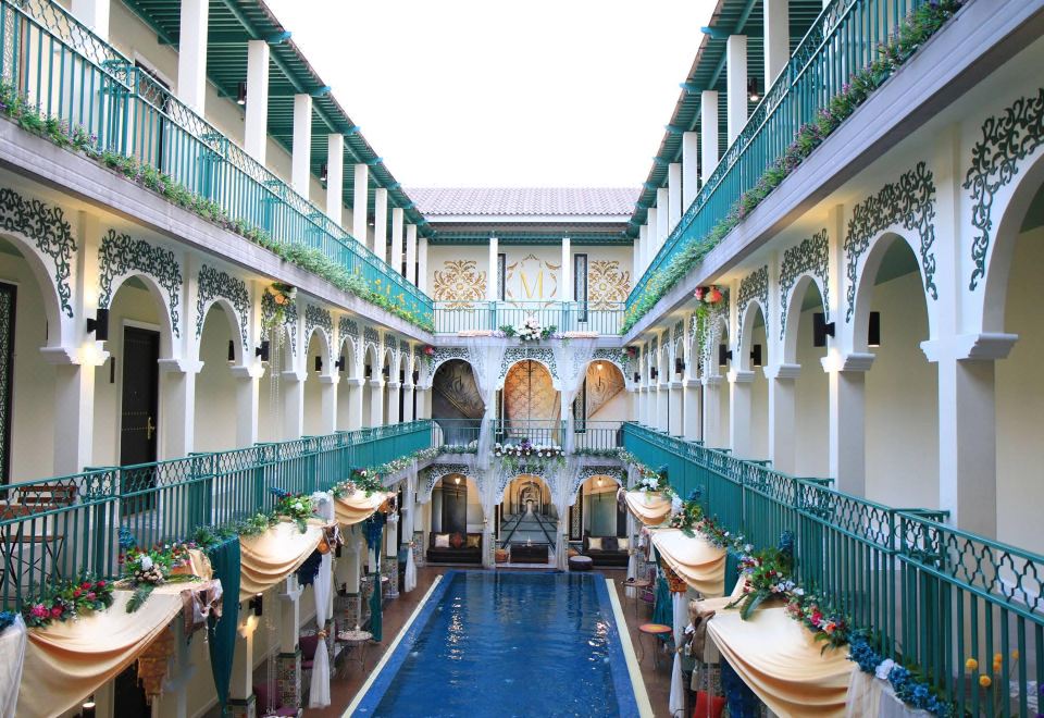 a large , ornate building with a blue swimming pool in the center , surrounded by tables and chairs at Palette the Grand Morocc Hotel