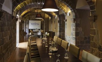 a long dining table with chairs and wine glasses is set up in a room with stone walls at Novotel Cusco