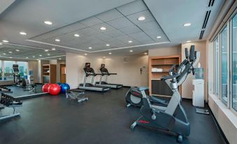 a gym with various exercise equipment , including treadmills and stationary bikes , under bright lights from ceiling lights at Fairfield by Marriott San Salvador