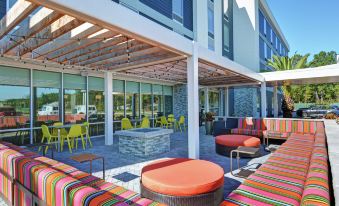 a modern outdoor living area with colorful furniture and a large , white building in the background at Home2 Suites by Hilton Richmond Hill Savannah I 95