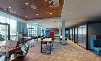 a modern office space with large windows , wooden ceiling , and various seating arrangements including tables and chairs at Village Hotel Farnborough