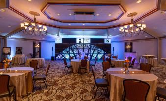 a large room with tables and chairs , a stage at the end , and chandeliers hanging from the ceiling at SureStay Plus Hotel by Best Western Lehigh Valley