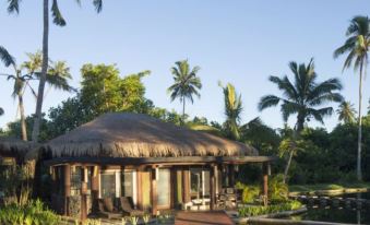 a large , thatched - roof building with a walkway leading to it , surrounded by lush greenery and palm trees at Coconuts Beach Club Resort and Spa
