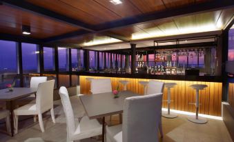 a restaurant with white chairs and tables , a bar , and a view of the ocean at ASTON Imperial Bekasi Hotel & Conference Center