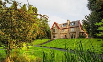 a large stone house surrounded by a lush green lawn , with trees and bushes in the background at Balcary House Hotel