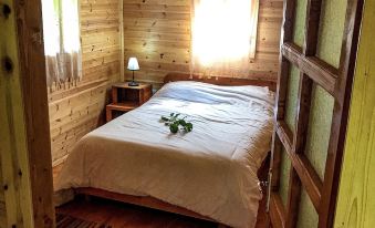 a cozy bedroom with wooden walls , a white bedspread , and green plants on the bedside table at Farma Sotira