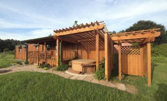 a wooden gazebo surrounded by green grass and trees , with a hot tub in the background at BlissWood B&B Ranch