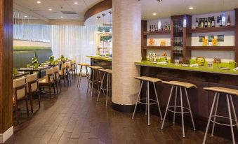 a well - lit restaurant with wooden floors , white walls , and an open kitchen area , featuring various dining tables and chairs at Aloft Miami Dadeland