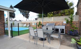 a patio with a table and chairs , an umbrella , and a pool in the background at Sandhurst Motor Inn Bendigo
