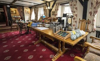 a large wooden dining table surrounded by chairs , with various items on the table and a red carpeted floor at Queens Head Inn