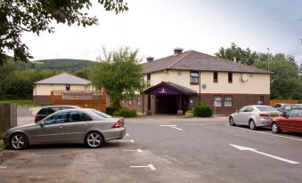 a parking lot with several cars , including a blue car and a white car , parked in front of a building at Premier Inn Caerphilly (Corbetts Lane)
