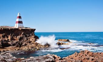 a lighthouse standing on a rocky shore with waves crashing against the rocks and a clear blue sky in the background at Robetown Motor Inn & Apartments