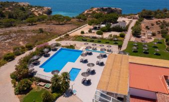aerial view of a resort with a pool surrounded by lounge chairs and umbrellas , located near the ocean at Vila Alba Resort
